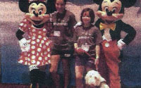 Newspaper clipping photo: two people posing with costumed Minnie and Mickey Mouse characters, a dog lying at their feet